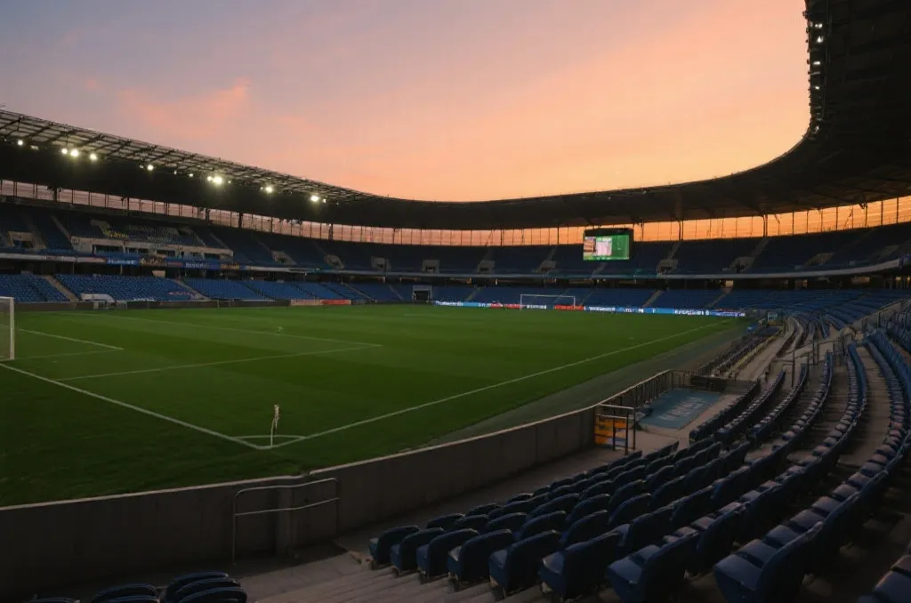 An empty modern soccer stadium bowl with thousands of seats under a dramatic sunset sky